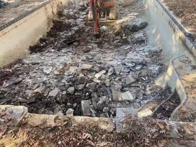 A Delaware backyard pool in the process of demolition by Remove A Pool, with heavy machinery breaking apart the concrete structure.