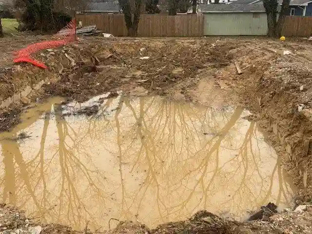 An excavated site in Dallas, Texas, after a pool demolition by Remove A Pool, with rainwater collecting in the empty space.