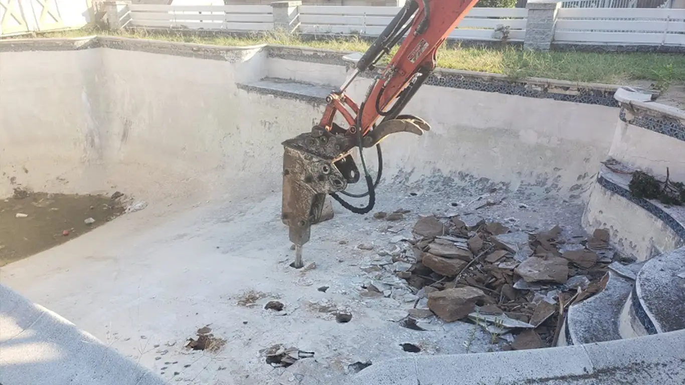 Pool Removal Annapolis MD - Excavator breaking down the concrete structure of a pool during removal.