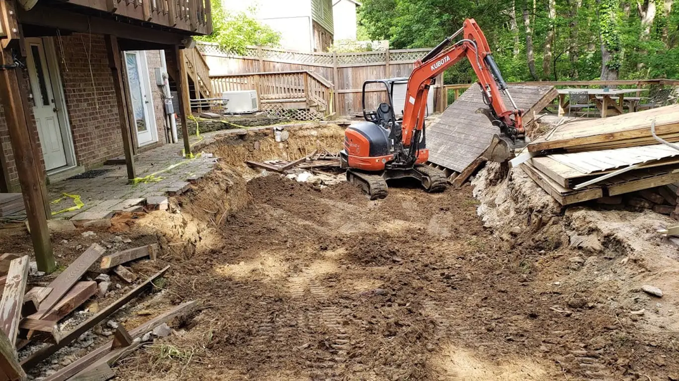 An orange Kubota excavator is seen working in a backyard, removing debris from a recently demolished pool. Pool Removal Virginia a project of Remove A Pool.