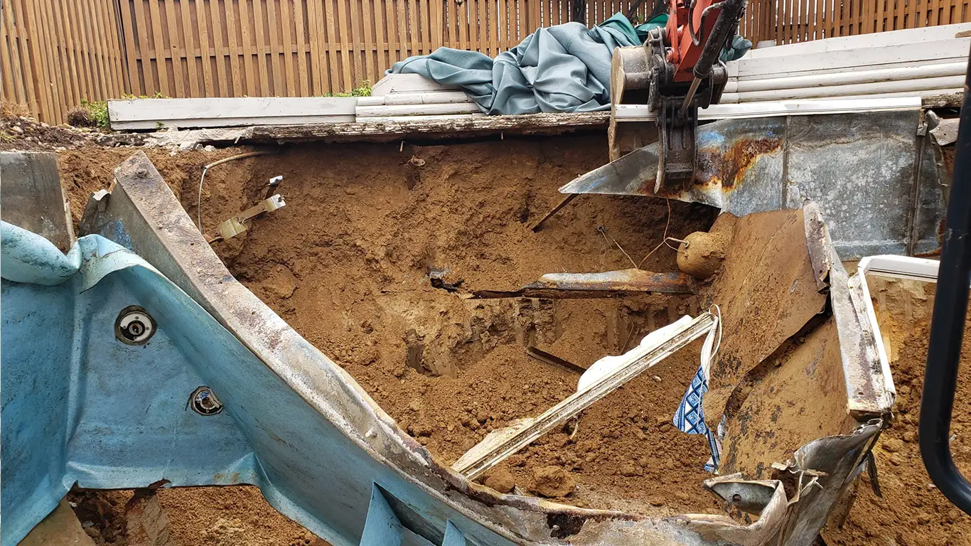 An inground pool removal process in progress in Arizona, showing the pool structure being demolished with heavy equipment by Remove A Pool. Rusted and damaged pool walls are being excavated and filled with dirt. This image highlights affordable pool demolition services for inground pools, ideal for those searching for 'pool removal near me' or 'inground pool removal' in Arizona.