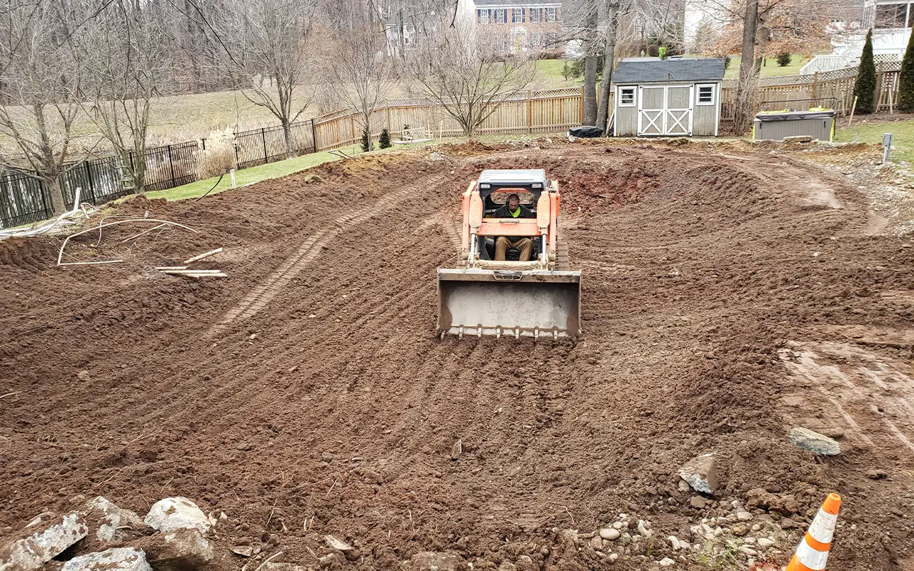 An Arlington VA pool removal project by Remove A Pool, featuring a bulldozer leveling the ground after the pool has been removed in a residential backyard.