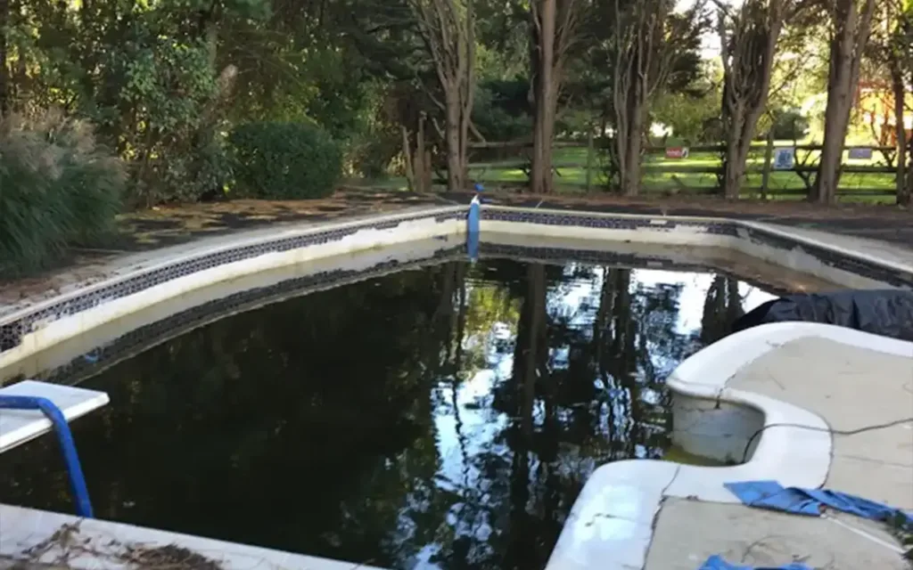 A neglected swimming pool in Dallas with dark, murky water, set for Dallas pool demolition and removal by Remove A Pool.