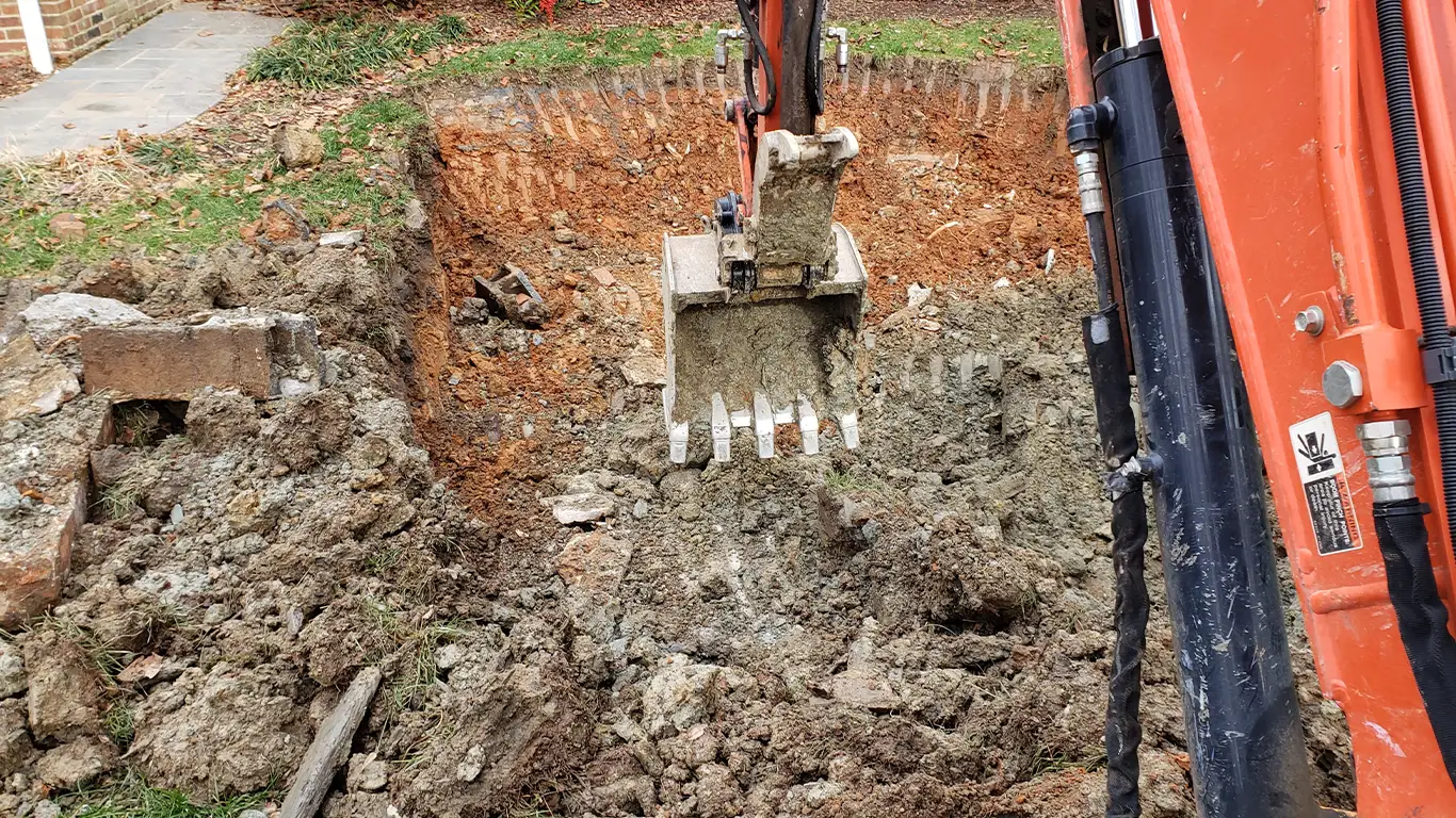 The image shows an excavator digging up concrete and soil during a pool removal in Newcastle, DE. The area is filled with debris from the removed pool, with heavy machinery actively working on the excavation. This scene highlights the process of pool removal Newcastle DE.