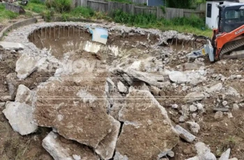 The client's yard is being prepared for restoration. A technician operates an excavator to remove pool debris during the pool removal process.