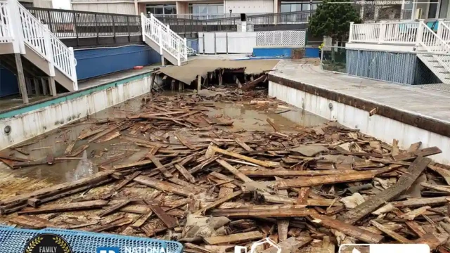 Demolition debris from a wooden deck filling a drained swimming pool, preparing for pool removal at a residential complex.