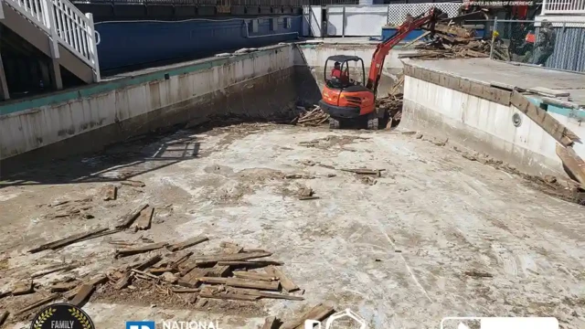 An excavator in a large drained commercial pool clearing out the remaining wooden debris before breaking up the pool structure.