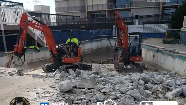 Two Kubota excavators breaking apart a concrete pool with large rock piles forming inside the pool area.