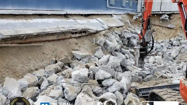 Heavy machinery breaking through thick concrete layers at the pool site with large rocks scattered around.