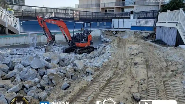 Tracks from machinery on the sand-filled pool area, with excavators clearing debris from the site.